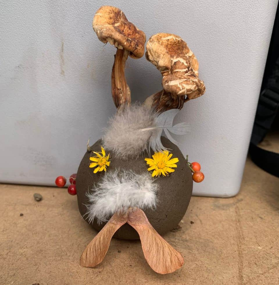 Mushroom and feather art display with flowers and natural elements, inspired by orchard scenery.