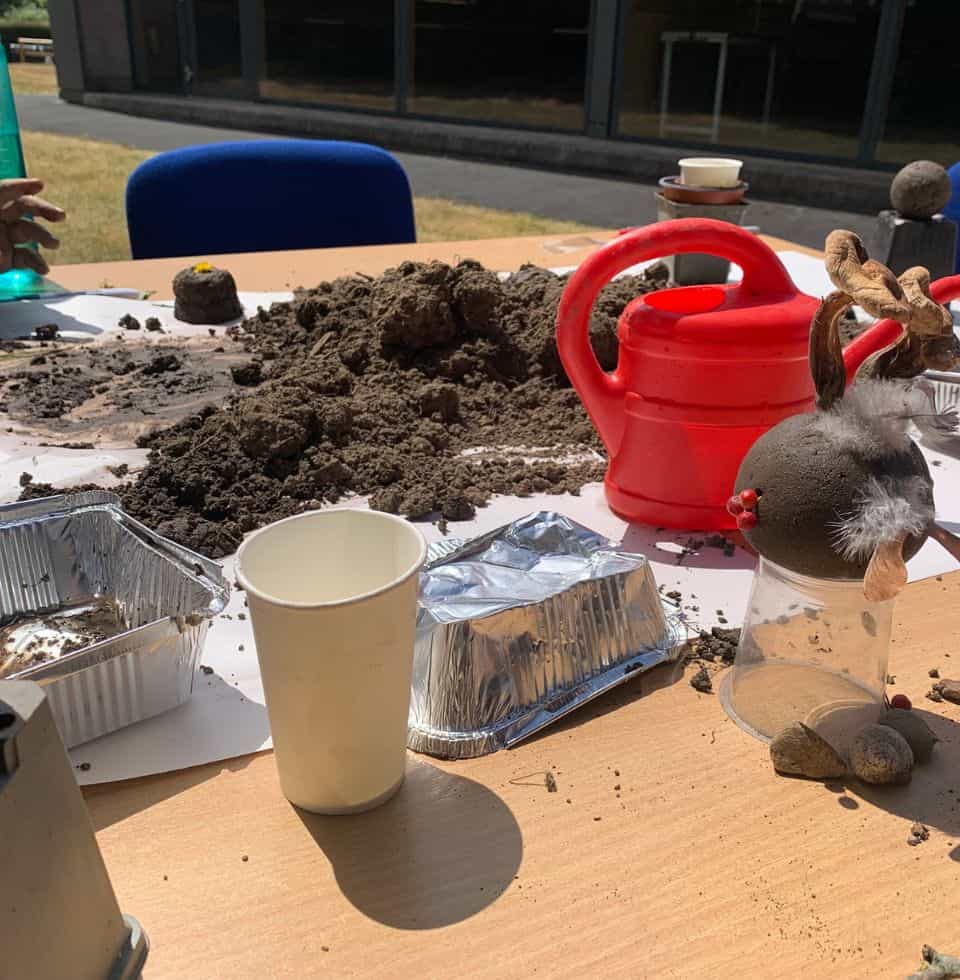 Colorful garden scene featuring soil, gardening tools, and decorative ornaments on a table.